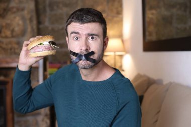 Kapalı ağızlı ve elinde sandviçle yakışıklı bir gencin yakın plan portresi.