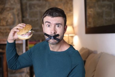 Kapalı ağızlı ve elinde sandviçle yakışıklı bir gencin yakın plan portresi.