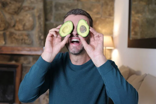 Evinde iki parça avokado tutan yakışıklı genç adamın yakın plan portresi.