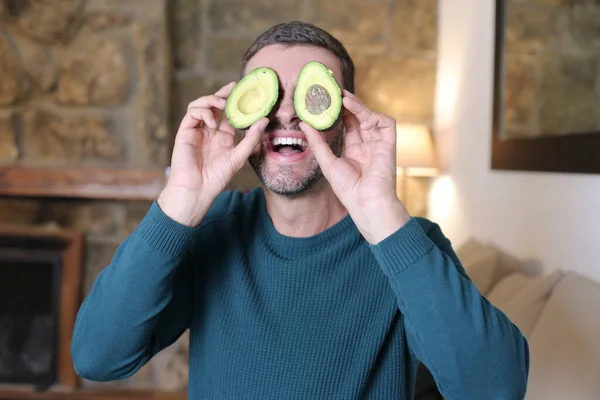 Evinde iki parça avokado tutan yakışıklı genç adamın yakın plan portresi.