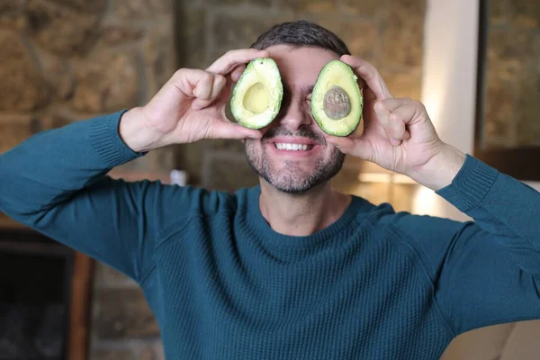 Evinde iki parça avokado tutan yakışıklı genç adamın yakın plan portresi.