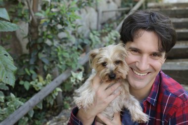 Küçük şirin bir köpek yavrusu tutan yakışıklı genç adamın portresi.