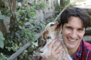 Küçük şirin bir köpek yavrusu tutan yakışıklı genç adamın portresi.