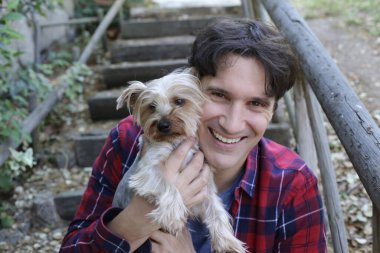 Küçük şirin bir köpek yavrusu tutan yakışıklı genç adamın portresi.