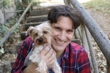 Küçük şirin bir köpek yavrusu tutan yakışıklı genç adamın portresi.