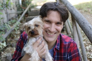 Küçük şirin bir köpek yavrusu tutan yakışıklı genç adamın portresi.