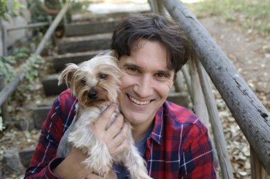 Küçük şirin bir köpek yavrusu tutan yakışıklı genç adamın portresi.