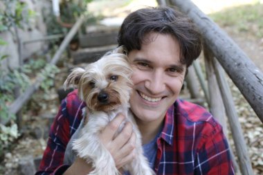 Küçük şirin bir köpek yavrusu tutan yakışıklı genç adamın portresi.