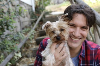 Küçük şirin bir köpek yavrusu tutan yakışıklı genç adamın portresi.