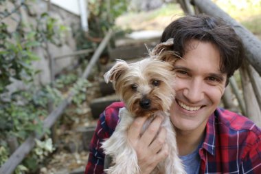 Küçük şirin bir köpek yavrusu tutan yakışıklı genç adamın portresi.