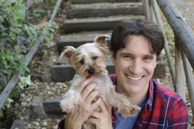 Küçük şirin bir köpek yavrusu tutan yakışıklı genç adamın portresi.