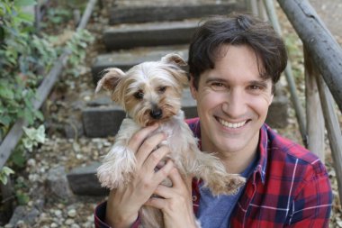 Küçük şirin bir köpek yavrusu tutan yakışıklı genç adamın portresi.