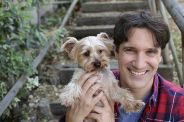 Küçük şirin bir köpek yavrusu tutan yakışıklı genç adamın portresi.