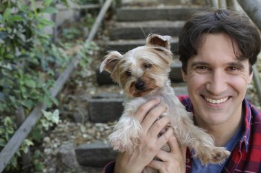 Küçük şirin bir köpek yavrusu tutan yakışıklı genç adamın portresi.