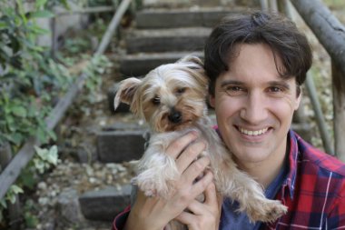 Küçük şirin bir köpek yavrusu tutan yakışıklı genç adamın portresi.