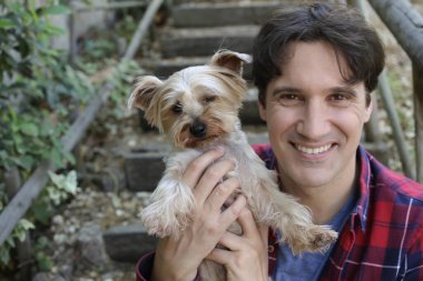 Küçük şirin bir köpek yavrusu tutan yakışıklı genç adamın portresi.