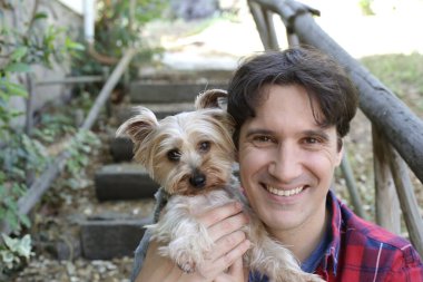 Küçük şirin bir köpek yavrusu tutan yakışıklı genç adamın portresi.