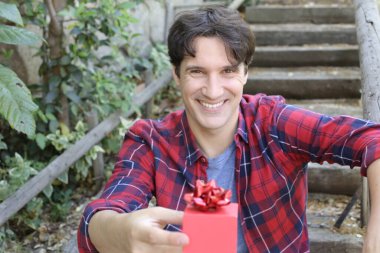 Elinde kırmızı hediye kutusu olan yakışıklı bir gencin portresi.