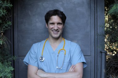 Gri duvarda steteskobu olan yakışıklı genç doktorun portresi.