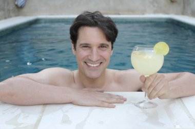 Yüzme havuzunda kokteyl içen yakışıklı genç adamın portresi.