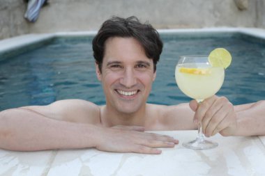 Yüzme havuzunda kokteyl içen yakışıklı genç adamın portresi.