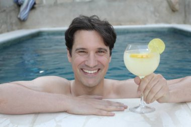 Yüzme havuzunda kokteyl içen yakışıklı genç adamın portresi.