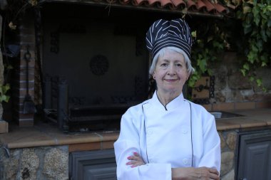 Şef üniformalı, şapkalı olgun bir kadının yakın plan portresi.