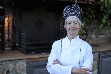 Şef üniformalı, şapkalı olgun bir kadının yakın plan portresi.