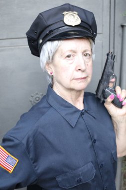Gri duvar arkasında, polis üniformalı olgun bir kadının yakın plan portresi.