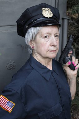 Gri duvar arkasında, polis üniformalı olgun bir kadının yakın plan portresi.