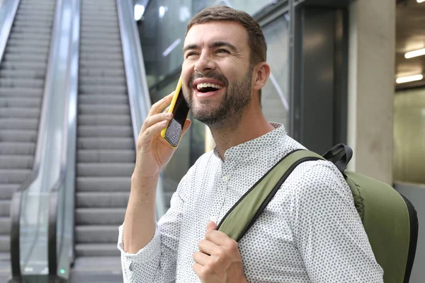 close-up portrait of handsome young man with backpack talking by phone on train station during trip