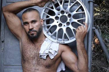 Gri duvarın önünde direksiyon sallayan yakışıklı, üstsüz genç adamın yakın plan portresi.