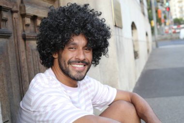 close-up portrait of handsome young curly man sitting on city street