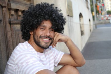 close-up portrait of handsome young curly man sitting on city street