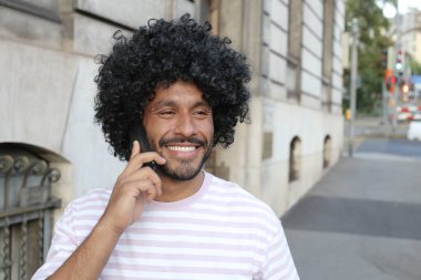 close-up portrait of handsome young curly man talking by phone on city street