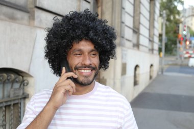 close-up portrait of handsome young curly man talking by phone on city street