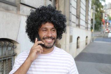 close-up portrait of handsome young curly man talking by phone on city street