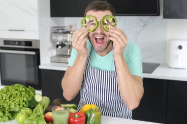 Evde yemek pişirirken sebzelerle oynayan yakışıklı genç adamın portresi.