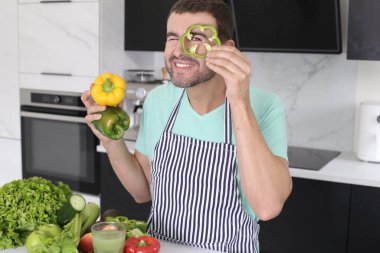 Evde yemek pişirirken sebzelerle oynayan yakışıklı genç adamın portresi.