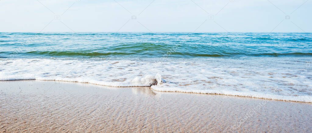 A coastal stone, washed by the waves, on a sandy beach on the shore against a blurry background of the sea