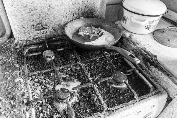 Dirty sporák and broken chicken egg on it, pan with fried egg and sweet pepper, black and white photo — Stock fotografie