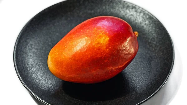 Fresh juicy red-orange mango on a black plate isolated on a white background, close-up — Stock Photo, Image