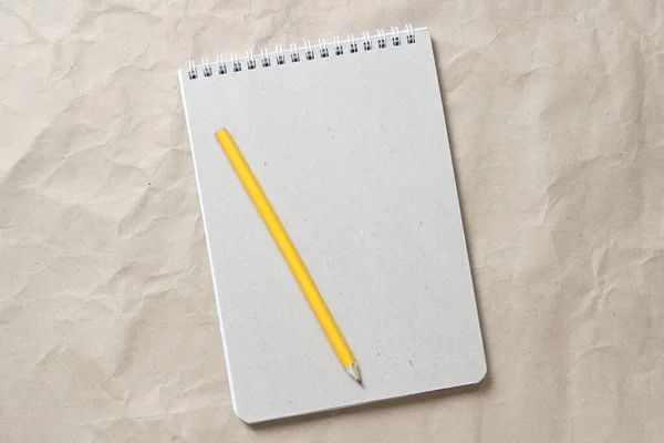 Серый блокнот с белой рулонной пружиной и карандашом на фоне бежевой ручной бумаги — стоковое фото