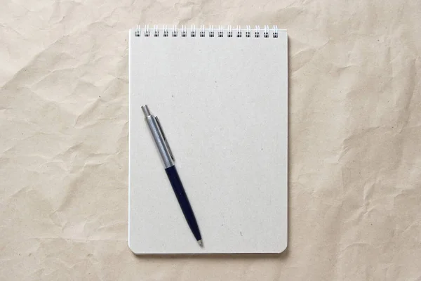 Bloc de notas gris con muelle en espiral blanco y pluma sobre un fondo de papel artesanal arrugado beige —  Fotos de Stock
