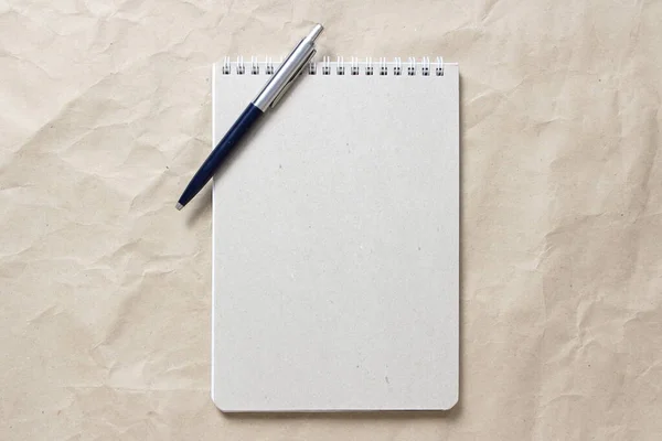 Bloc-notes gris avec ressort enroulé blanc et stylo sur fond de papier artisanal froissé beige — Photo