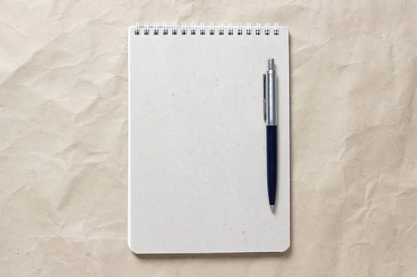 Bloc-notes gris avec ressort enroulé blanc et stylo sur fond de papier artisanal froissé beige — Photo