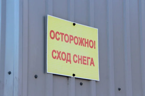 Напис на тарілці: увага, падає сніг. Обережно, сніг падає з дахів, попереджаючи на стіні. Пересторога на ярлику російською — стокове фото