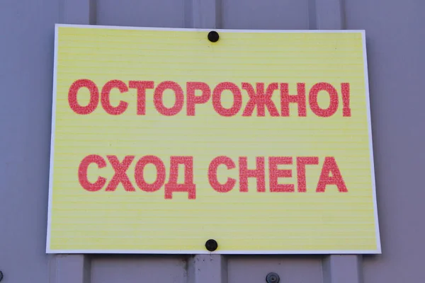 Напис на тарілці: увага, падає сніг. Обережно, сніг падає з дахів, попереджаючи на стіні. Пересторога на ярлику російською — стокове фото