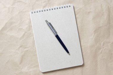  Beyaz sarmalanmış yay ve arkaplandaki bej buruşuk el işi kağıdının üzerindeki kalemle gri not defteri.