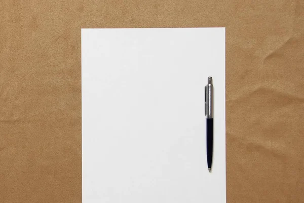 Modelo de papel branco com caneta encontra-se no fundo de pano marrom claro. Conceito de plano de negócios e estratégia. Foto stock com espaço vazio para texto e design — Fotografia de Stock